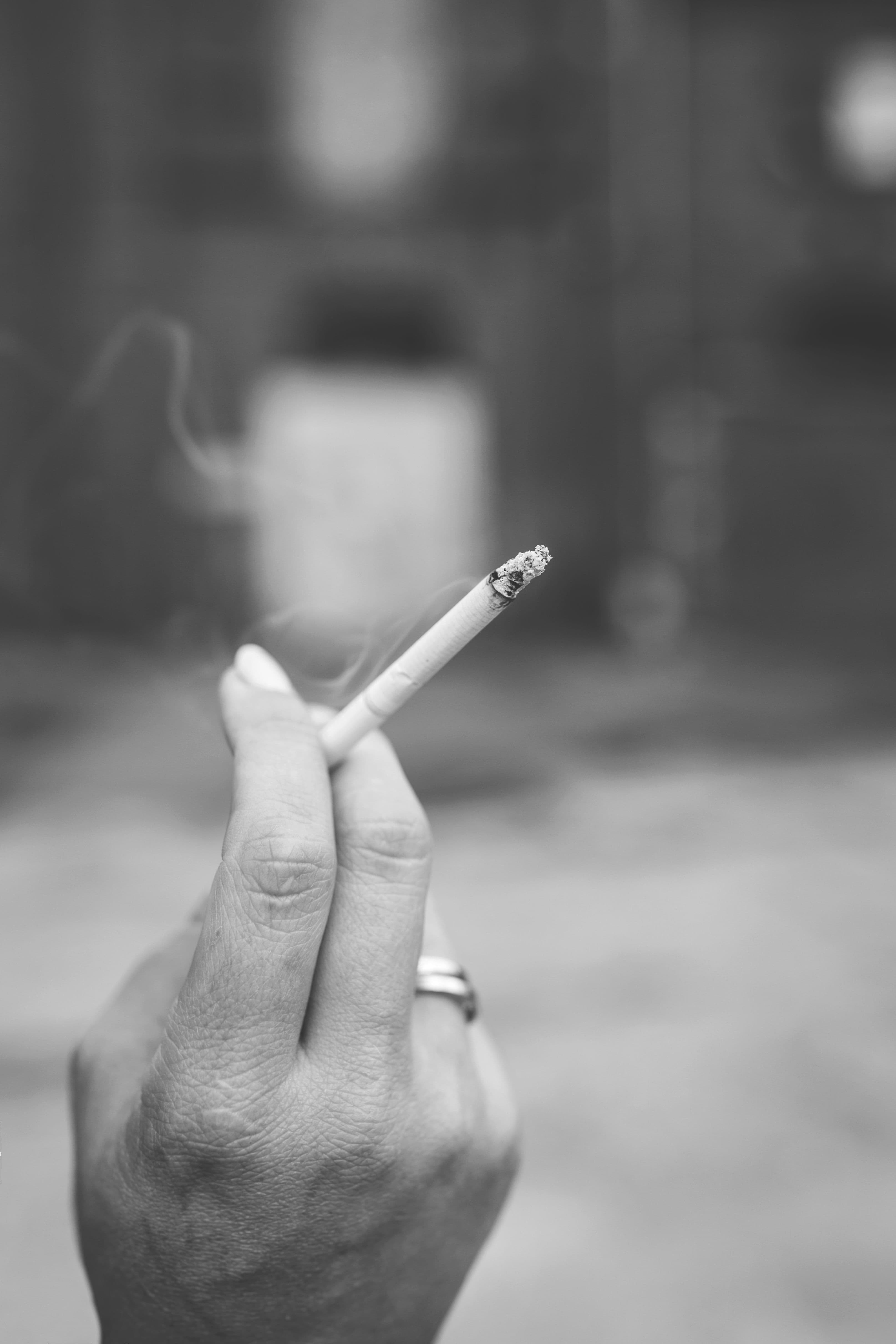 A hand holding a lit cigarette, with smoke curling upward