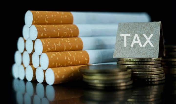 Stacked cigarettes beside stacked coins and a sign reading "TAX"