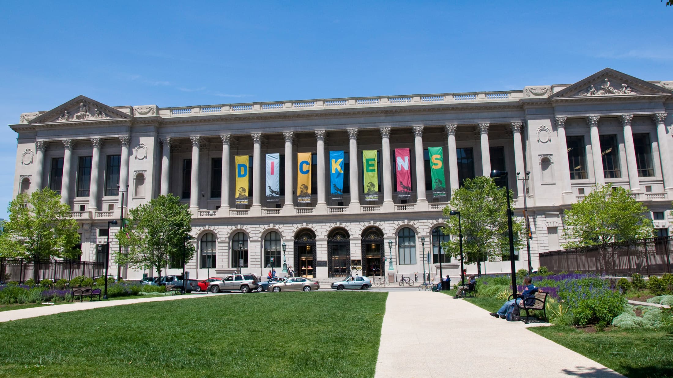 A grand public library interior with towering columns and multiple levels of bookshelves, with readers at tables on the ground floor